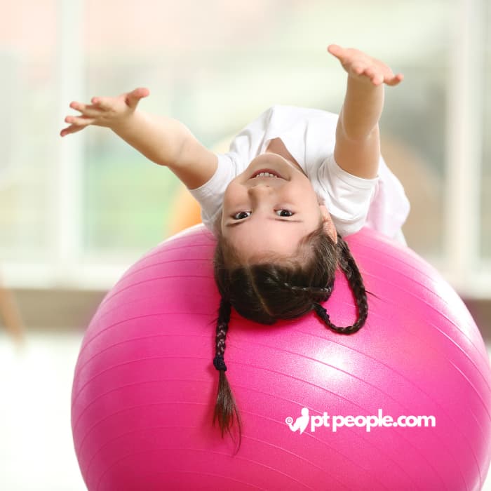 Child learning tumbling moves with a supportive gymnastics instructor.