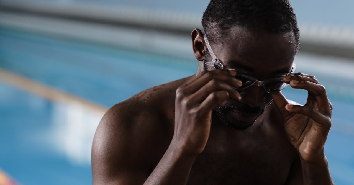 A focused athlete preparing for swimming in an indoor pool by adjusting his goggles.