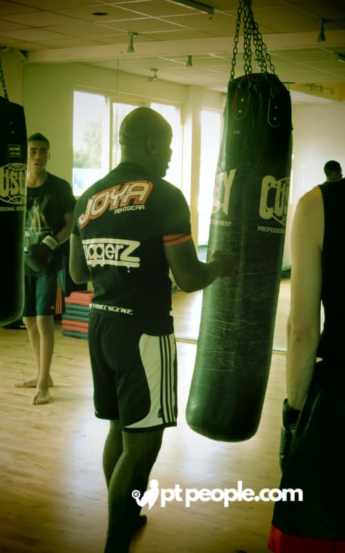 Male PT in Dubai boxing gloves hitting a punching bag during a boxing lesson. (This describes a solo training scene, uses the location "Dubai" and the keyword "boxing lessons", and emphasizes a popular training method for building strength and endurance).