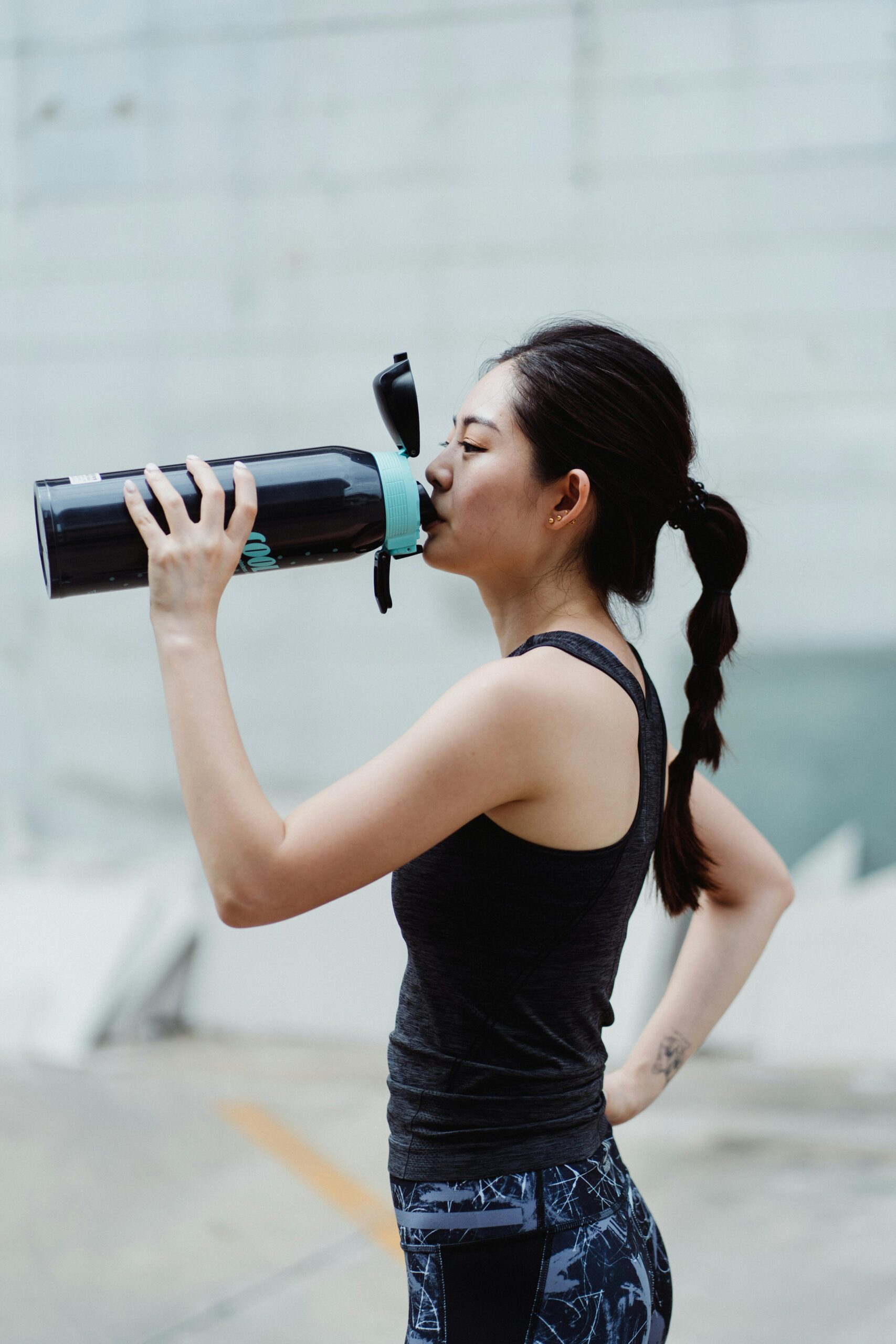 Asian woman taking a break to hydrate during an outdoor summer workout session.