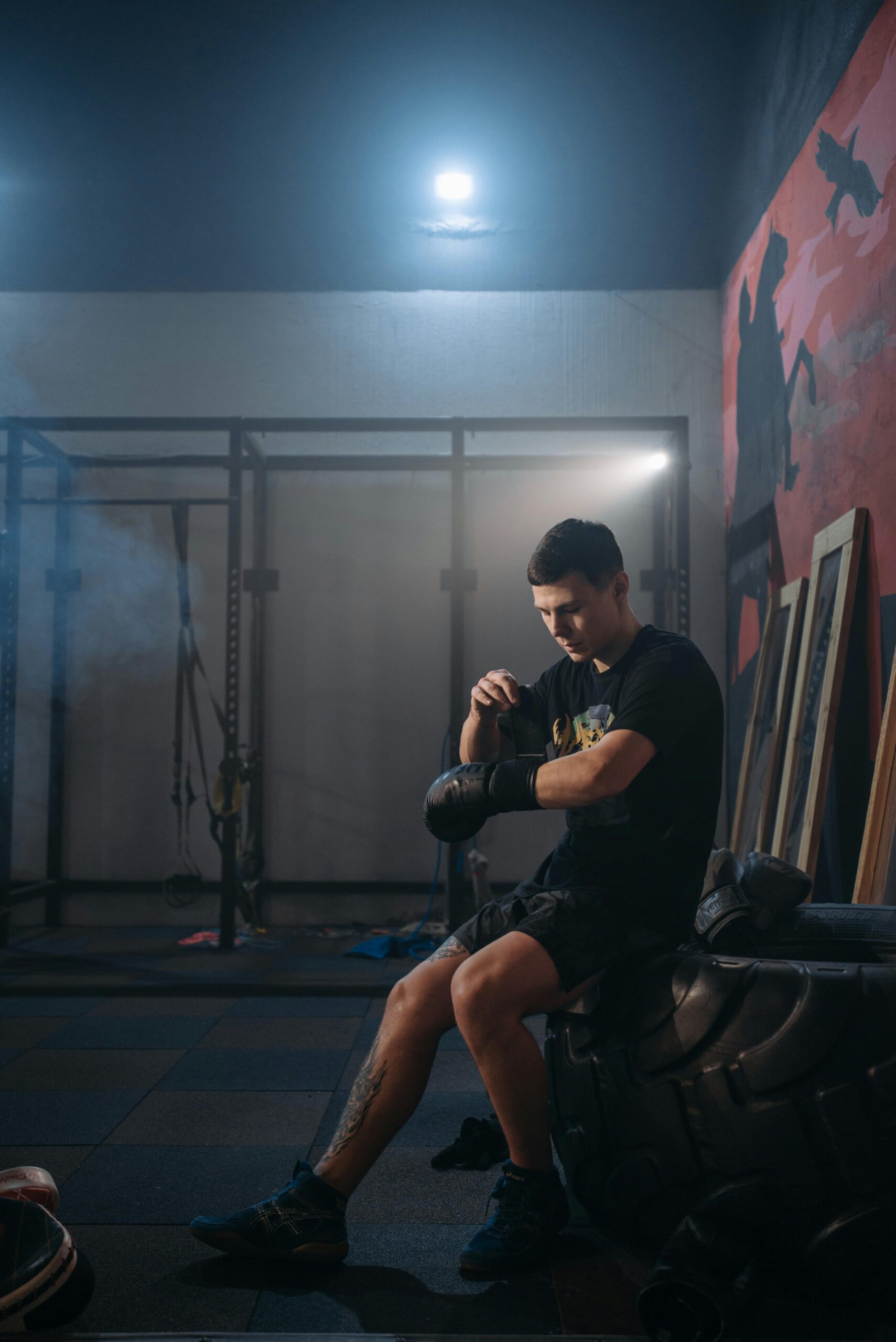 A male boxer takes a break in a dimly lit gym, preparing for intense training.