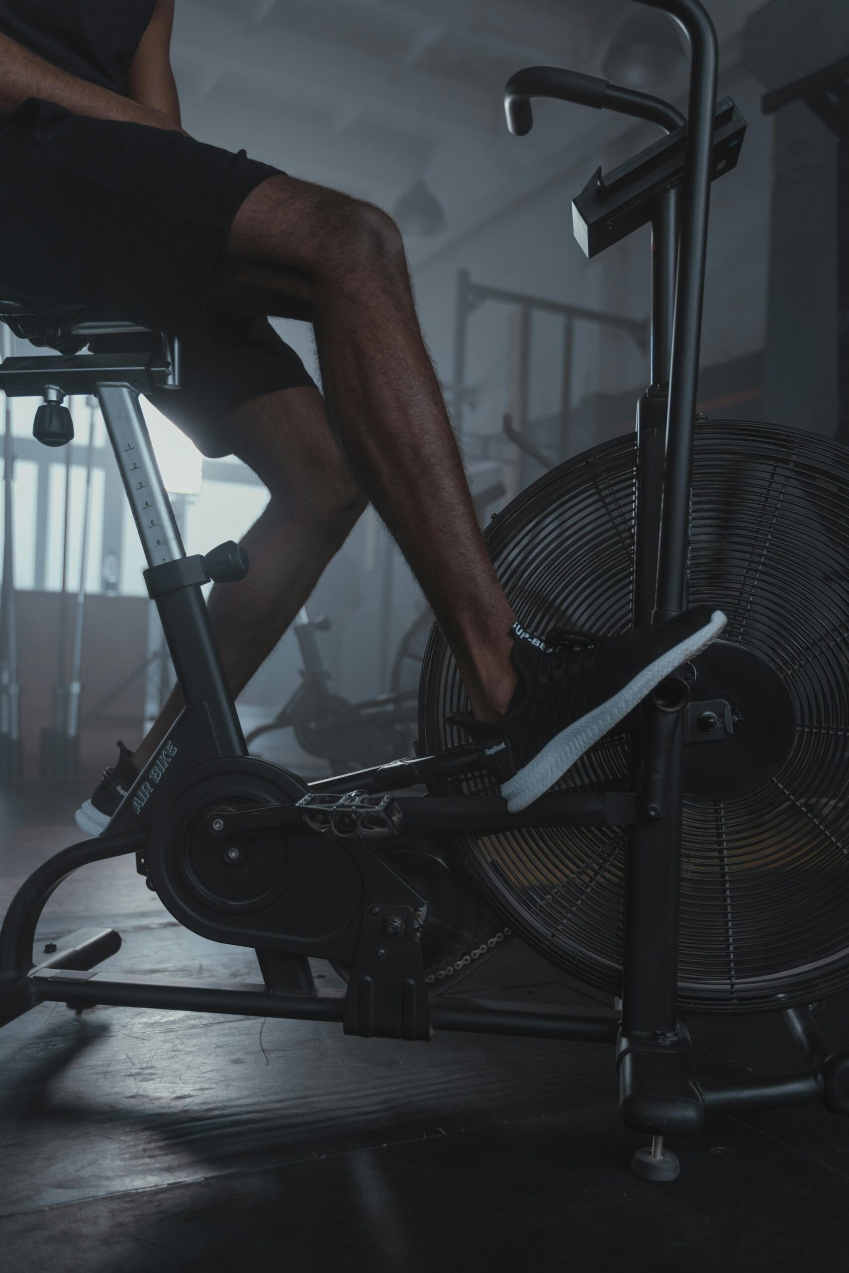 Close-up of a man working out on a stationary bike indoors with gym equipment around.