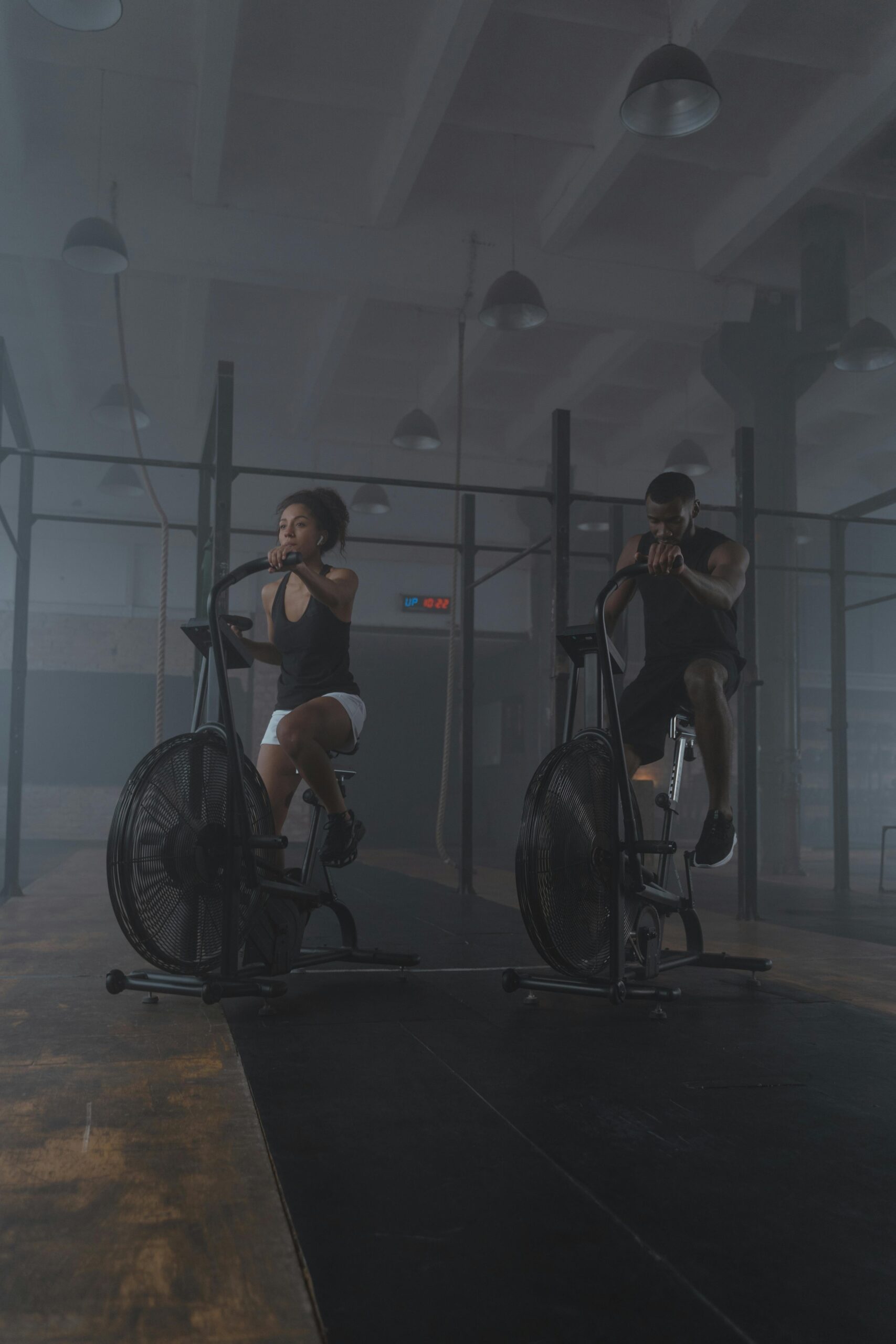 A focused pair of athletes exercising on air bikes, showcasing endurance and fitness in a gym setting.