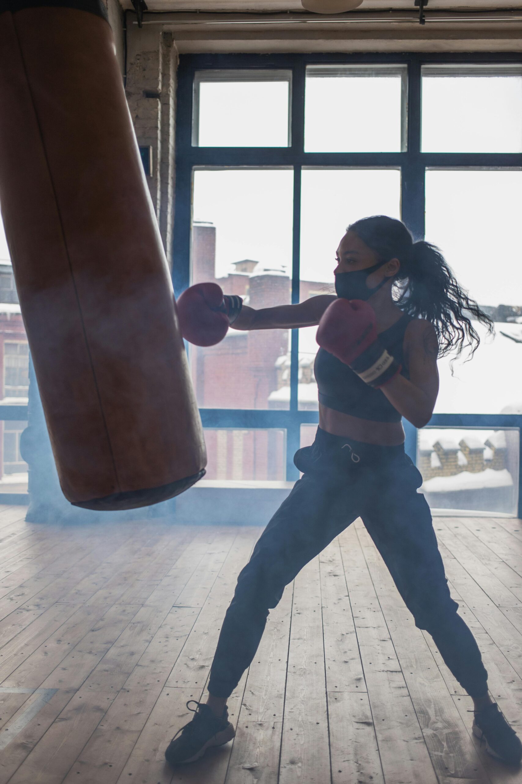 A woman boxer in a mask trains with a punching bag indoors, exemplifying focus and strength.