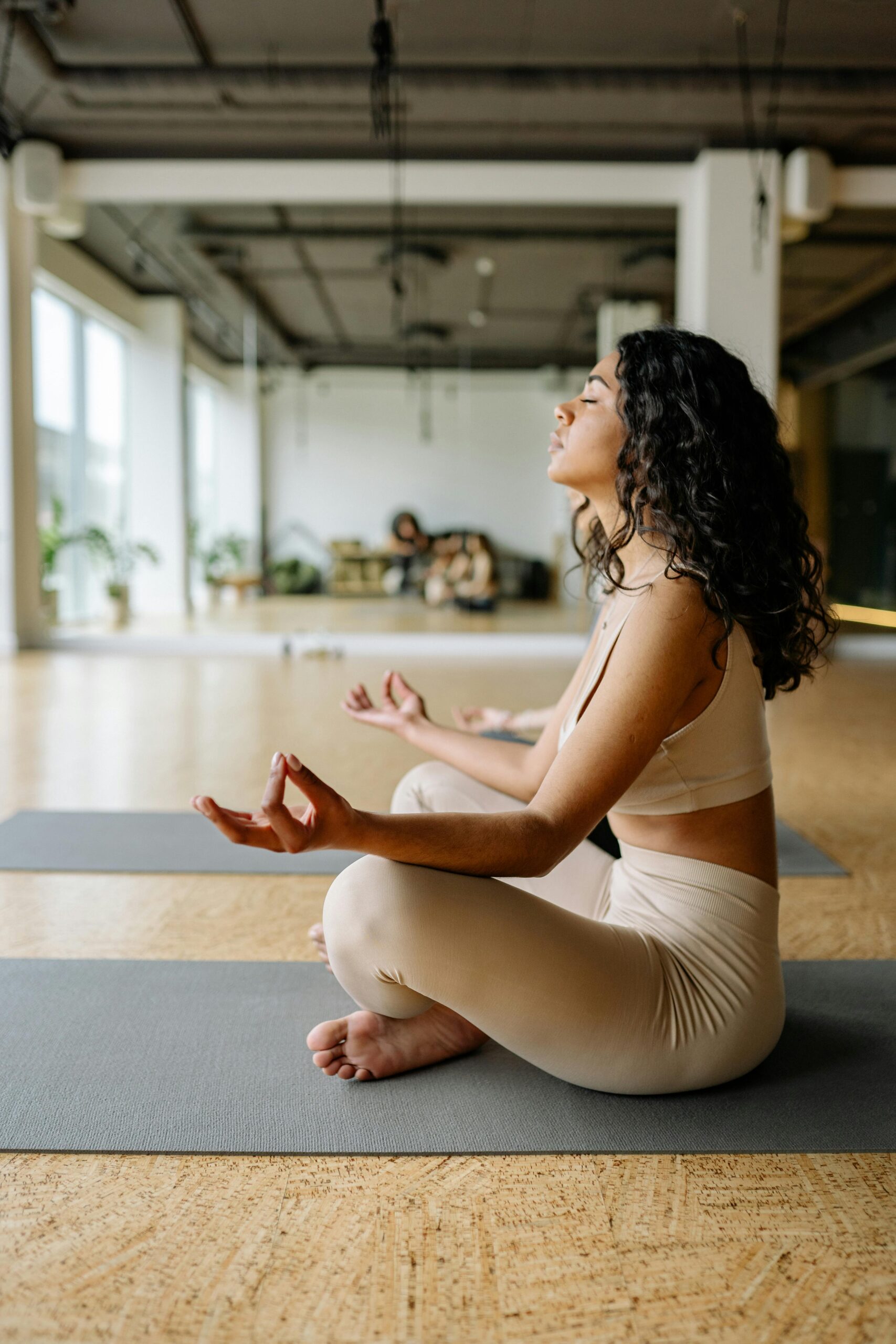 A young woman in a yoga pose practicing meditation inside a modern gym setting.